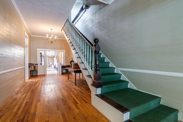 staircase featuring a chandelier, wood-type flooring, and ornamental molding