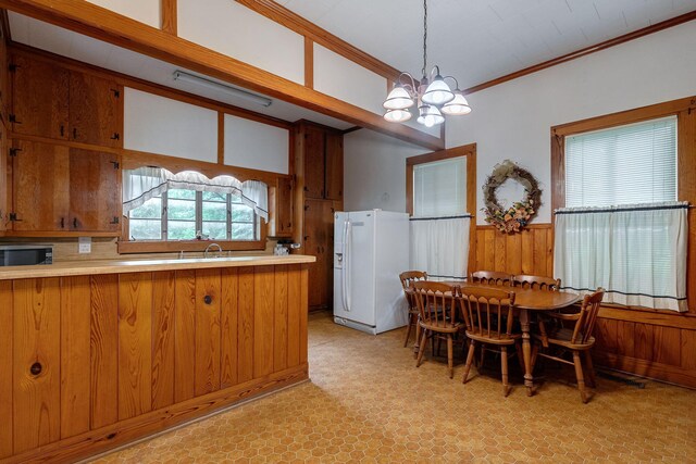 dining room featuring wood walls, sink, crown molding, and an inviting chandelier