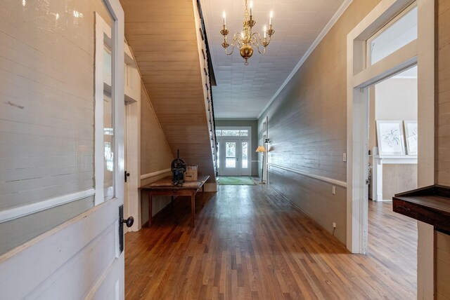 corridor featuring hardwood / wood-style flooring, crown molding, and an inviting chandelier