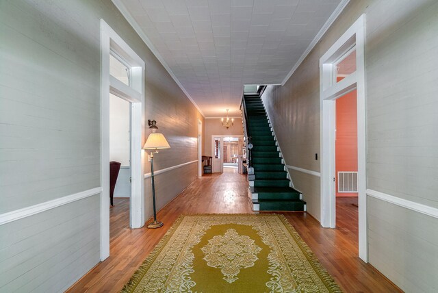 hallway with hardwood / wood-style flooring, an inviting chandelier, and crown molding