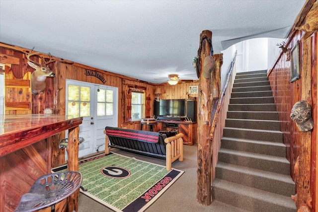 interior space with a textured ceiling, carpet floors, ceiling fan, and wooden walls