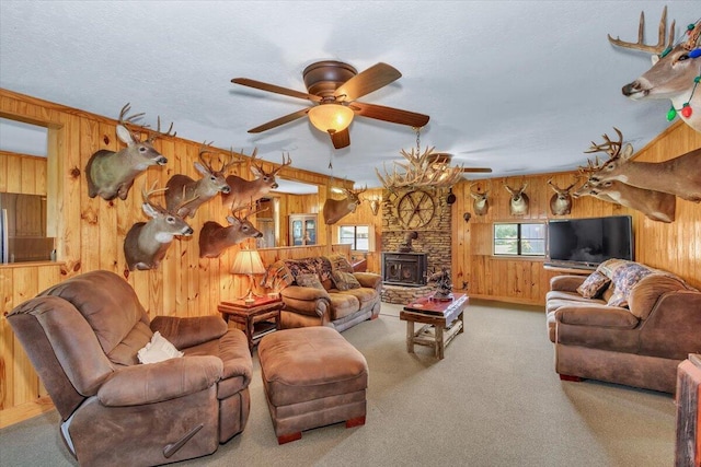 carpeted living room with ceiling fan, a wood stove, a textured ceiling, and wooden walls