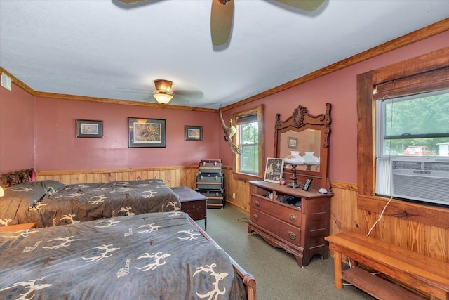 carpeted bedroom with multiple windows, wood walls, ceiling fan, and ornamental molding