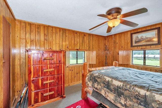 bedroom with carpet, ceiling fan, wood walls, and multiple windows