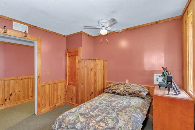 carpeted bedroom with ceiling fan, crown molding, and wooden walls