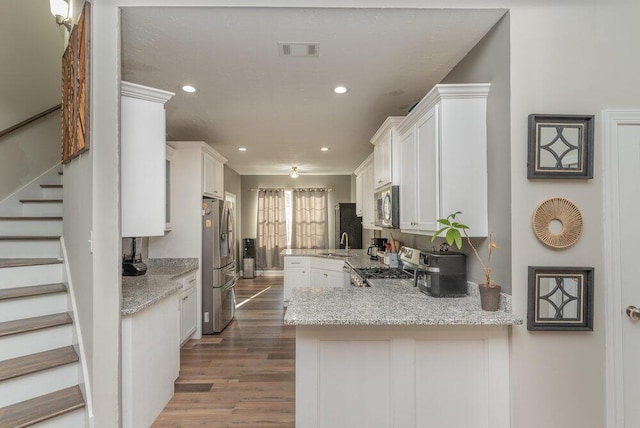 kitchen with dark wood-type flooring, appliances with stainless steel finishes, kitchen peninsula, and white cabinets