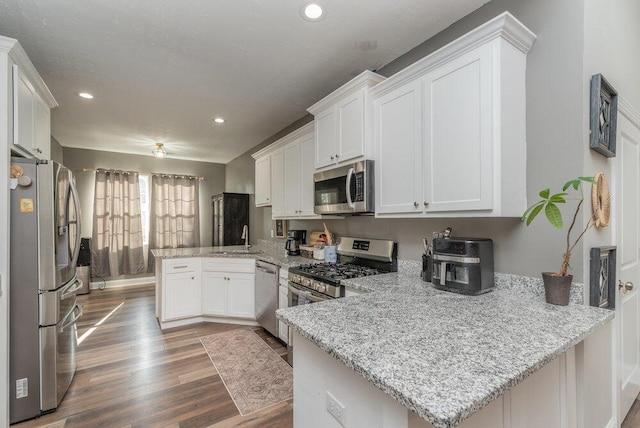 kitchen featuring stainless steel appliances, light stone countertops, white cabinets, and kitchen peninsula