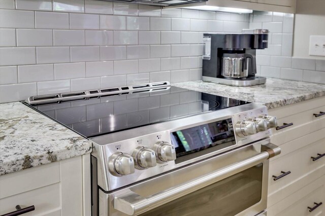 kitchen with decorative backsplash, light stone countertops, white cabinetry, and high end stainless steel range