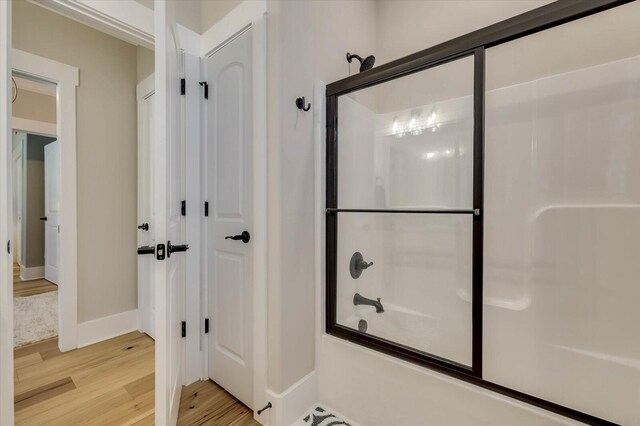 bathroom featuring hardwood / wood-style flooring and bath / shower combo with glass door