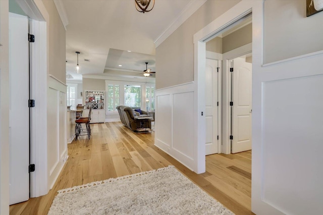 corridor with wood-type flooring, ornamental molding, and a tray ceiling