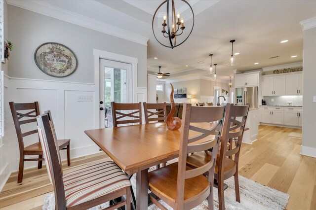 dining space with crown molding, sink, light hardwood / wood-style floors, and ceiling fan with notable chandelier