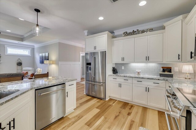 kitchen featuring light stone countertops, white cabinetry, hanging light fixtures, stainless steel appliances, and light wood-type flooring