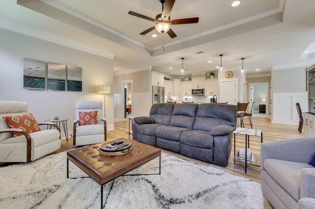 living room featuring a tray ceiling, crown molding, and light hardwood / wood-style floors