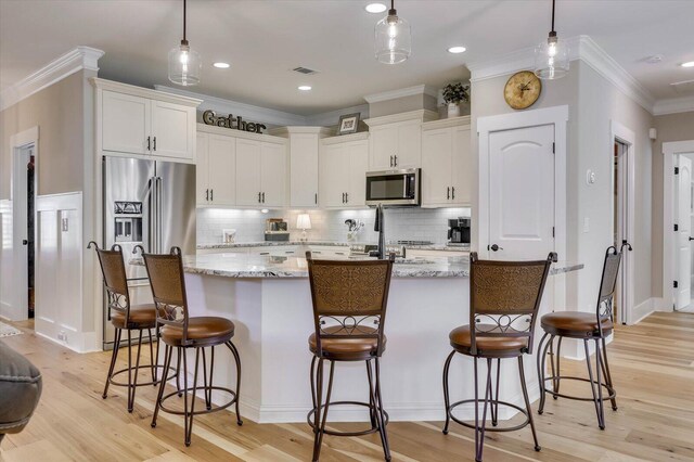 kitchen with light stone countertops, decorative light fixtures, stainless steel appliances, and a center island with sink