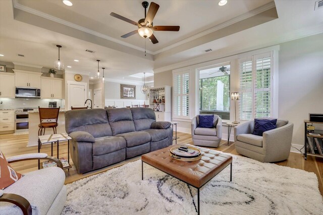 living room featuring a raised ceiling, ceiling fan, crown molding, and light hardwood / wood-style floors