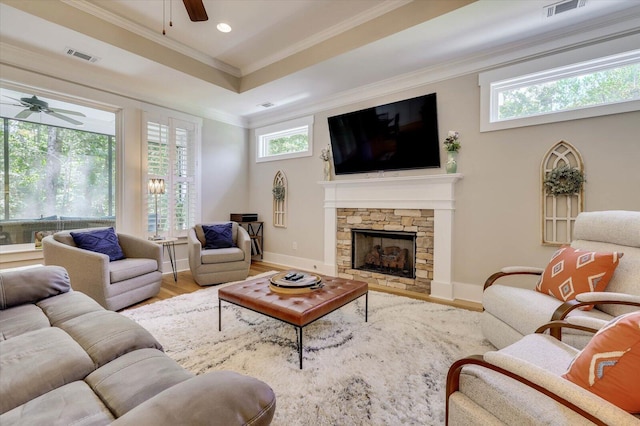 living room with a stone fireplace, ceiling fan, wood-type flooring, and ornamental molding