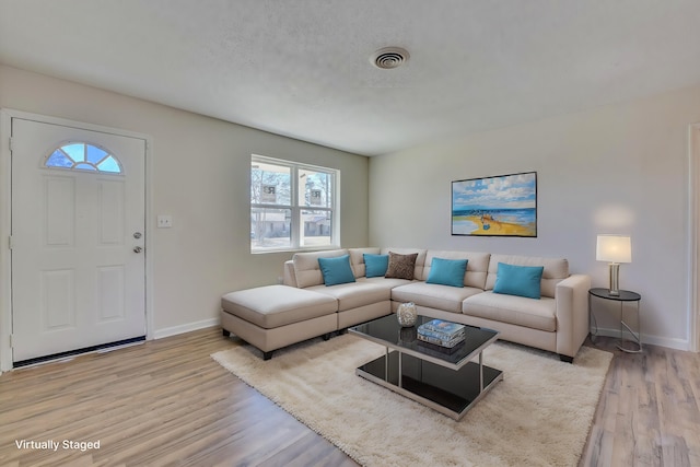 living room featuring light wood finished floors, baseboards, visible vents, and a textured ceiling