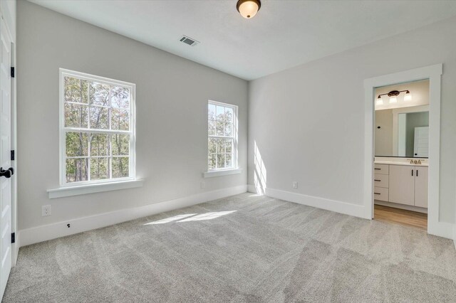 unfurnished bedroom with light colored carpet, ensuite bath, and sink