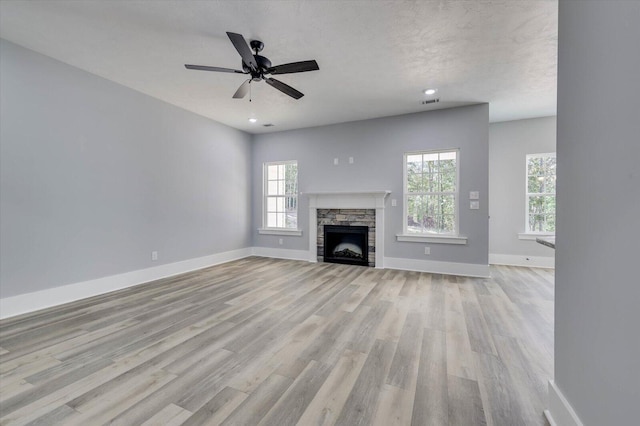 unfurnished living room with a stone fireplace, ceiling fan, light hardwood / wood-style flooring, and a textured ceiling