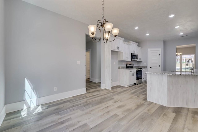 kitchen with appliances with stainless steel finishes, light wood-type flooring, light stone counters, white cabinets, and a chandelier