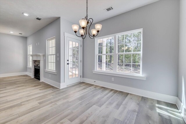 unfurnished dining area featuring a stone fireplace, light hardwood / wood-style floors, and an inviting chandelier