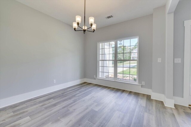 empty room with light wood-type flooring and a notable chandelier