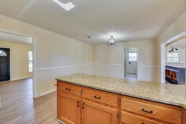 kitchen with a fireplace, light wood-style flooring, a textured ceiling, and light stone countertops