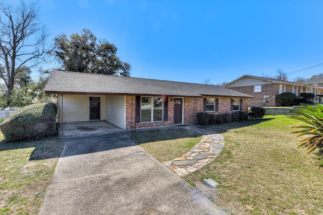 view of front facade with brick siding, roof with shingles, a front yard, an attached carport, and driveway