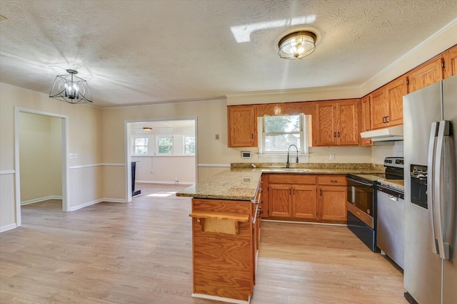 kitchen with brown cabinets, appliances with stainless steel finishes, a sink, a peninsula, and under cabinet range hood