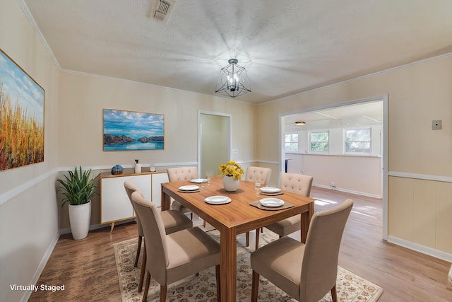 dining area with visible vents, wainscoting, crown molding, light wood-style floors, and a notable chandelier