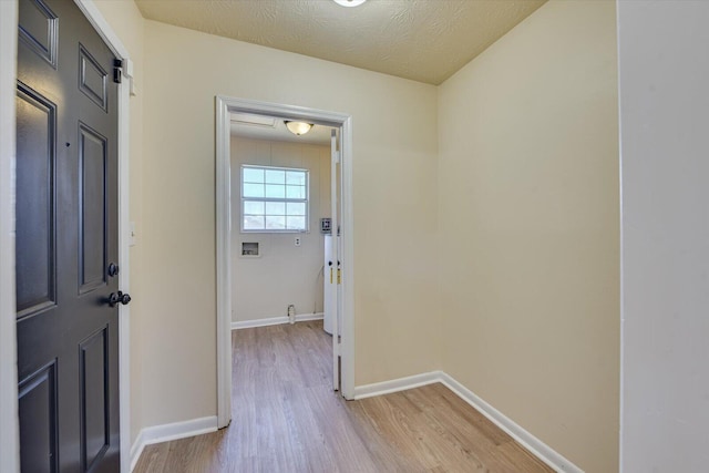 corridor featuring light wood-style floors, a textured ceiling, and baseboards