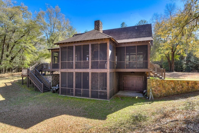 back of house with a garage, a sunroom, a yard, stairway, and a chimney