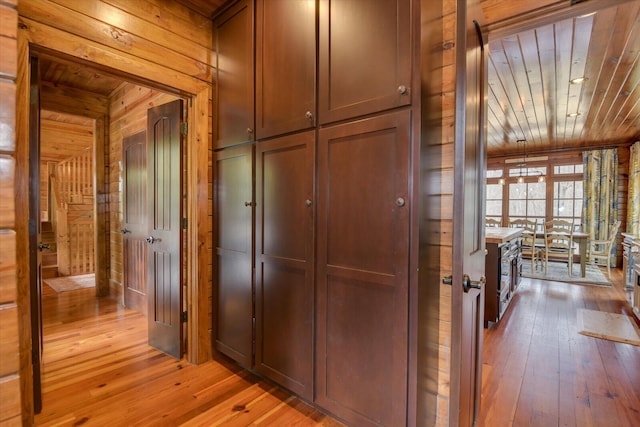 hallway with light wood-type flooring, wooden ceiling, and wood walls