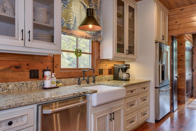 kitchen featuring stainless steel appliances, a sink, backsplash, light stone countertops, and glass insert cabinets