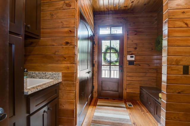 doorway to outside featuring visible vents, wood ceiling, light wood-style flooring, wood walls, and a sink