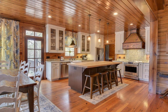 kitchen with stainless steel appliances, wood counters, light wood-style floors, a center island, and custom range hood