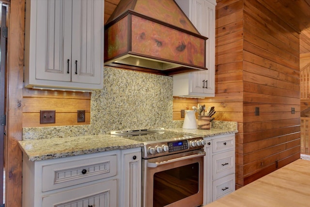 kitchen featuring wooden walls, white cabinets, custom exhaust hood, stainless steel range with electric stovetop, and backsplash