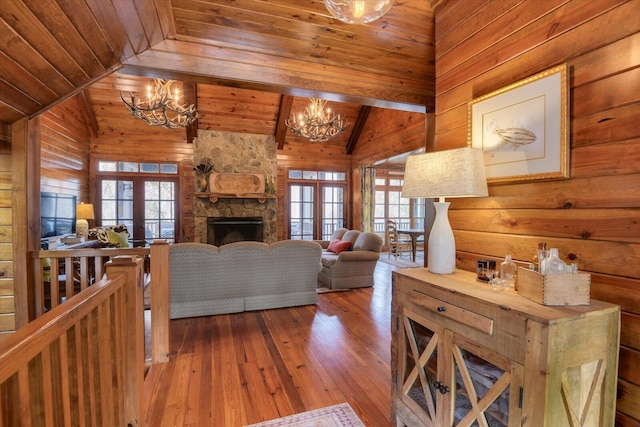 living area with vaulted ceiling with beams, wood ceiling, a stone fireplace, a chandelier, and hardwood / wood-style floors