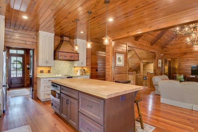 kitchen featuring light wood-style flooring, butcher block countertops, stainless steel appliances, wood walls, and premium range hood