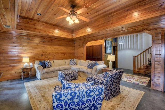 living room with finished concrete flooring, wooden walls, a ceiling fan, wood ceiling, and stairway