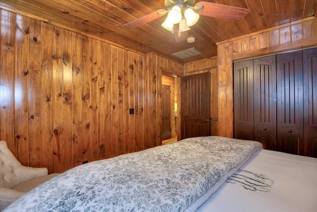 bedroom with visible vents, wooden ceiling, ceiling fan, wood walls, and a closet