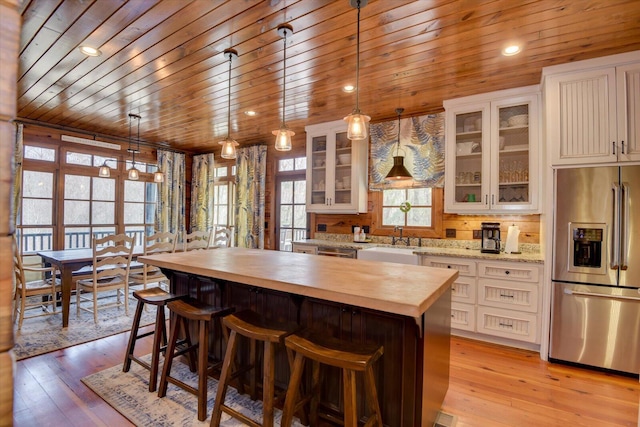 kitchen featuring stainless steel fridge with ice dispenser, butcher block countertops, a center island, light wood-type flooring, and a sink