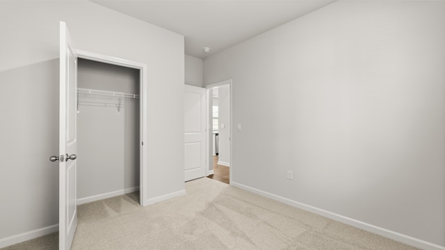 unfurnished bedroom with baseboards, a closet, and light colored carpet