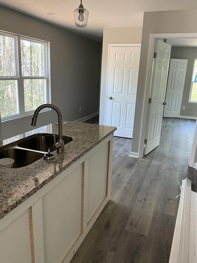 kitchen with light stone countertops, sink, white cabinets, and dark wood-type flooring