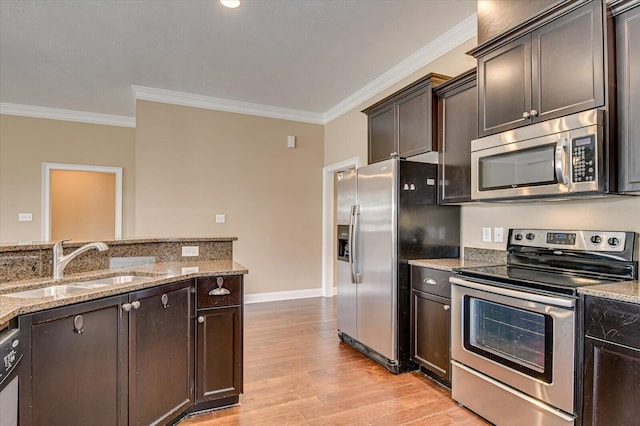 kitchen featuring light stone counters, light wood finished floors, stainless steel appliances, a sink, and dark brown cabinets