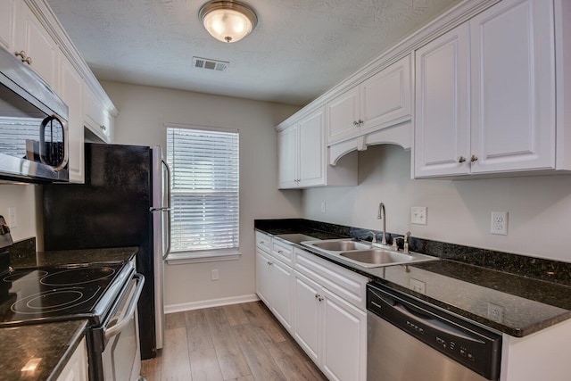 kitchen featuring sink, dark stone countertops, white cabinets, stainless steel appliances, and light hardwood / wood-style flooring