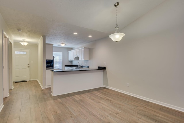 kitchen featuring lofted ceiling, light hardwood / wood-style floors, white cabinets, decorative light fixtures, and kitchen peninsula