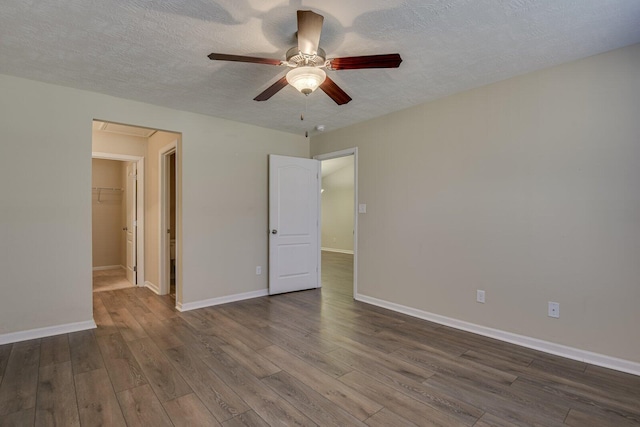 unfurnished bedroom featuring wood-type flooring, a spacious closet, a textured ceiling, a closet, and ceiling fan