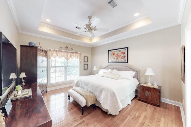 bedroom with light wood-style flooring, a raised ceiling, and visible vents