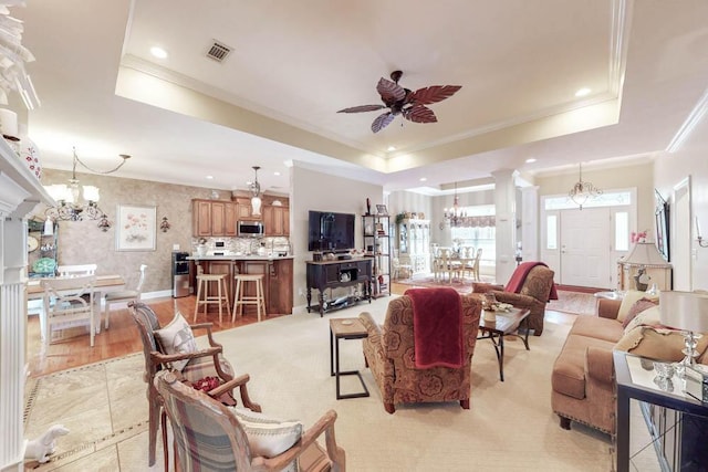 living area featuring ceiling fan with notable chandelier, a tray ceiling, decorative columns, and visible vents